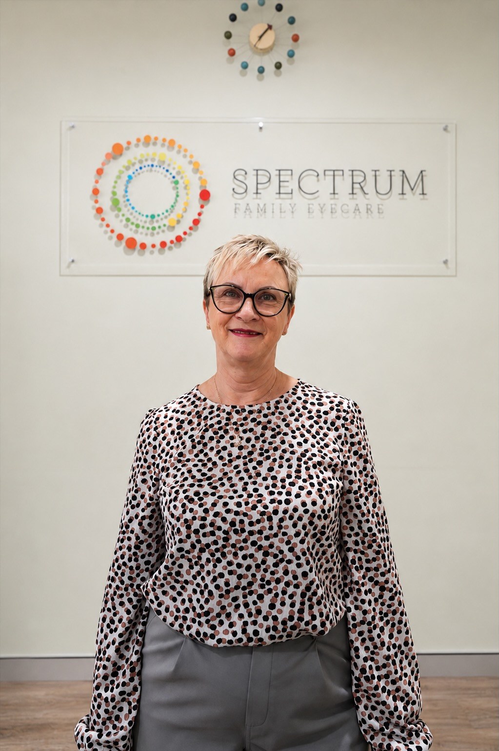 Gill, optical dispenser, standing in front of the Spectrum Family Eyecare signage wall.