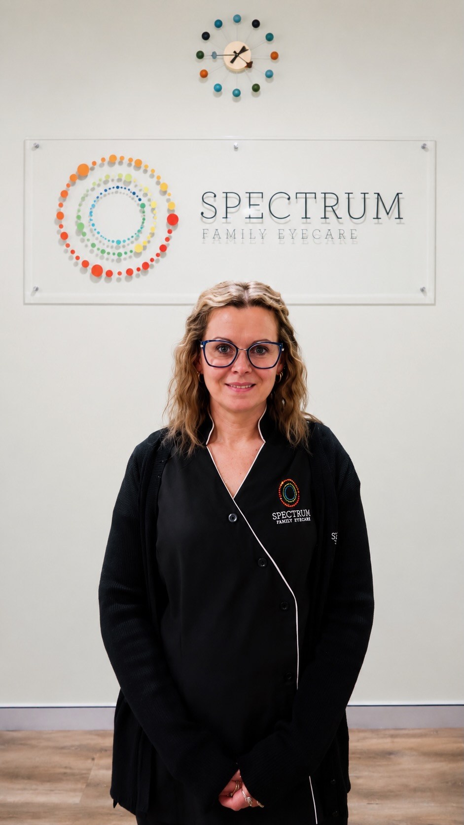 Megan, optical dispenser, standing in front of the Spectrum Family Eyecare signage wall.